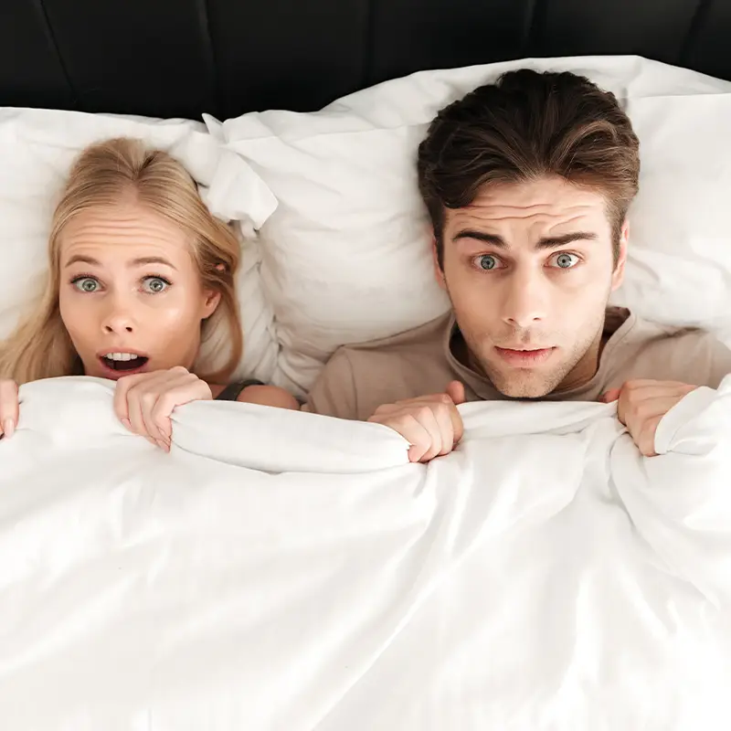 Couple under duvet representing discreet intimacy in shared homes and quiet environments