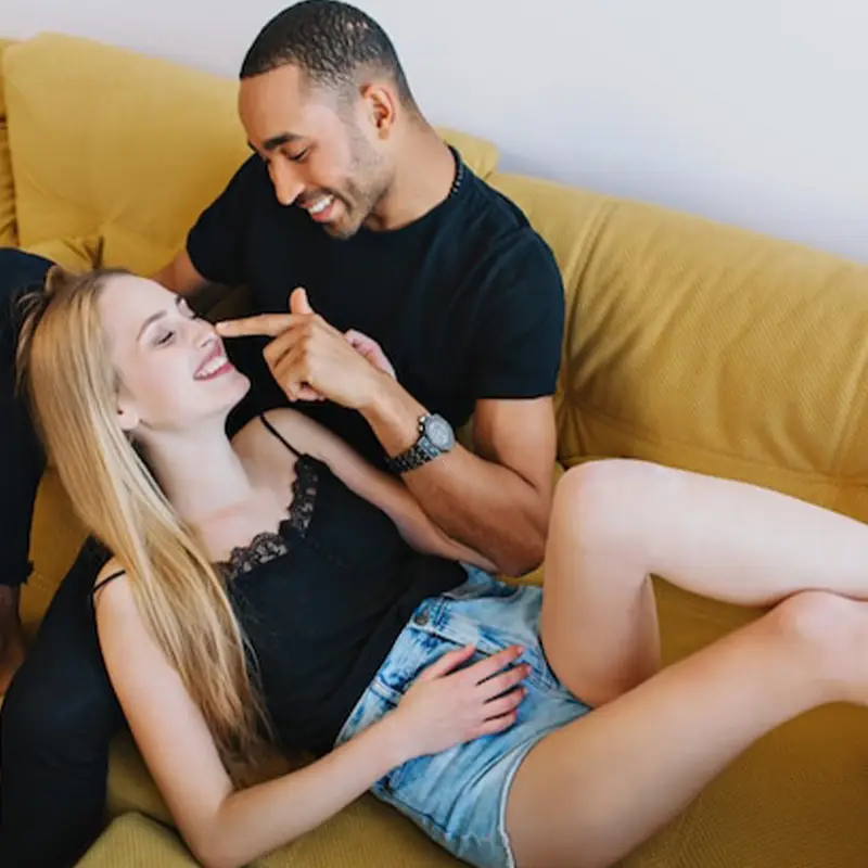 Relaxed couple laughing together on a sofa, showing playful intimacy and connection